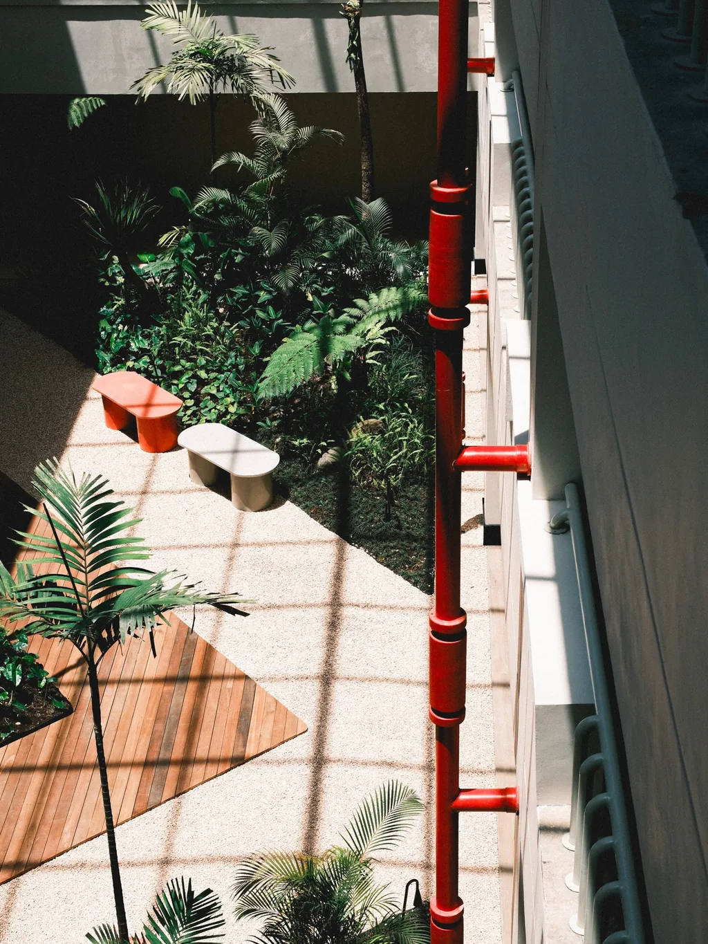 Atrium dilihat dari atas: tiang merah, dek kayu, pohon palem dan tanaman, dengan bangku dan kursi rendah