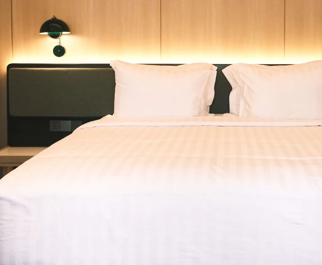 Kasur dengan sandaran hijau dan lampu dinding di kamar Bossa Nova