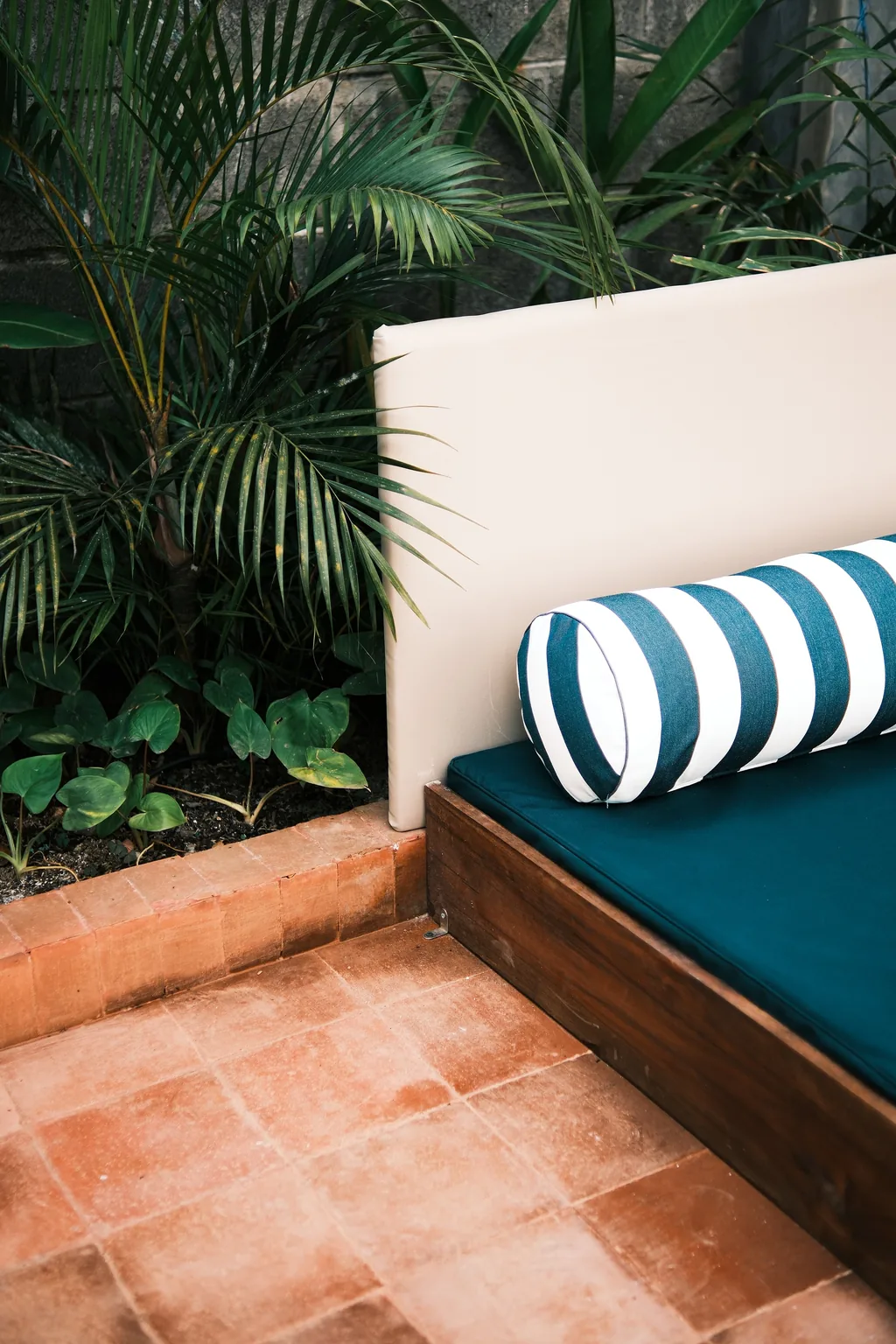 Daybed berbantal garis di teras terakota di antara pohon palem