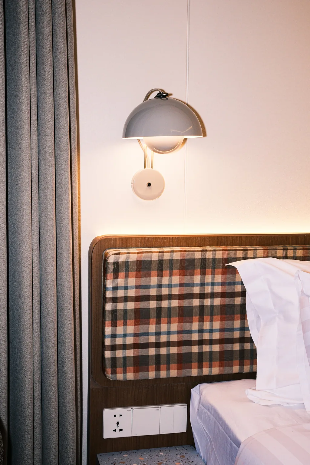 Sandaran kasur motif kotak-kotak dengan lampu dinding di kamar Volume Hotel