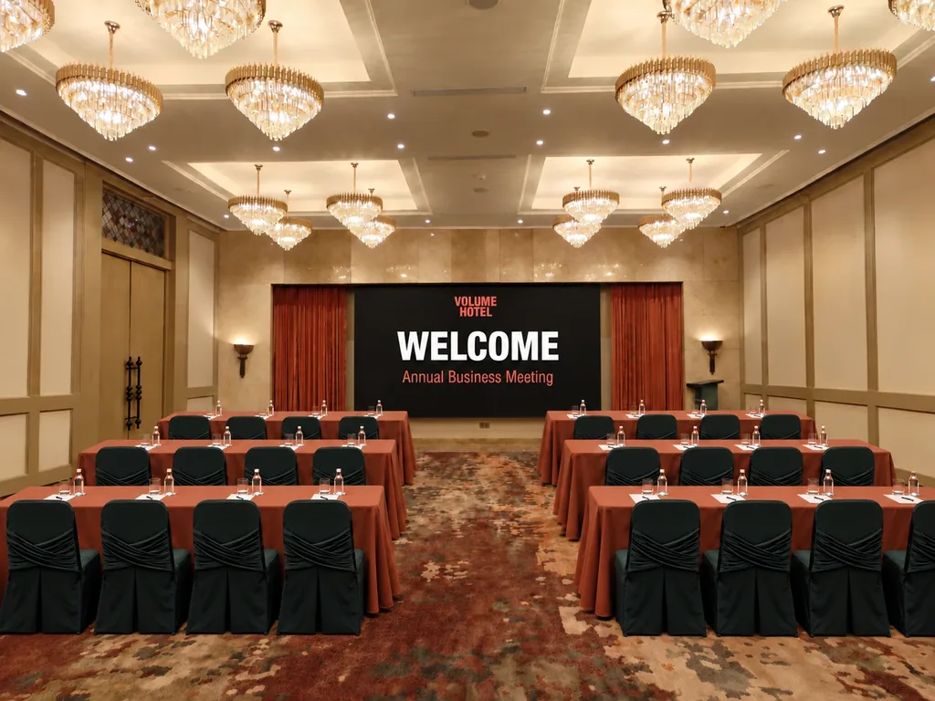 The Volume Hotel ballroom set up classroom-style for a meeting, with crystal chandeliers, terracotta table linen and the LED screen at the front